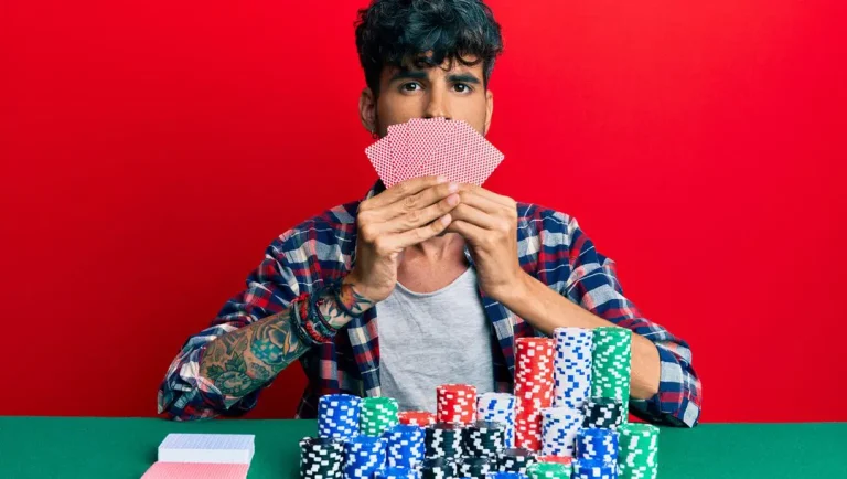 Young-man-playing-gambling-poker-covering-face-with-cards-against-a-red-background.-